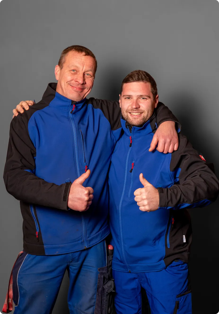 2 Mitarbeiter der Firma lächelnd, mit dem Daumen hoch, vor der Kamera stehend
